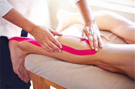 Physical therapist applying kinesiology tape to man's leg Stock Photo - Premium Royalty-Free, Code: 6113-08105486