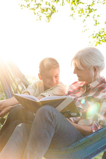 Grandmother reading to grandson in sunny hammock Stock Photo - Premium Royalty-Free, Image code: 6113-08220526