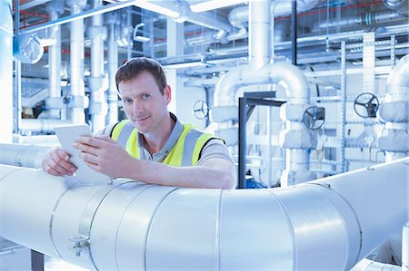 Portrait confident worker with digital tablet leaning on pipe in factory Stock Photo - Premium Royalty-Free, Code: 6113-08393677