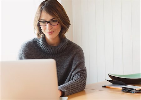 Brunette woman in sweater using laptop at table Stock Photo - Premium Royalty-Free, Code: 6113-08393689