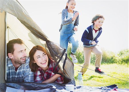 Smiling couple in tent watching kids running in grass Stock Photo - Premium Royalty-Free, Code: 6113-08393691