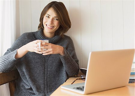 simsearch:6113-08393754,k - Portrait smiling brunette woman in sweater drinking coffee at laptop Stock Photo - Premium Royalty-Free, Code: 6113-08393739