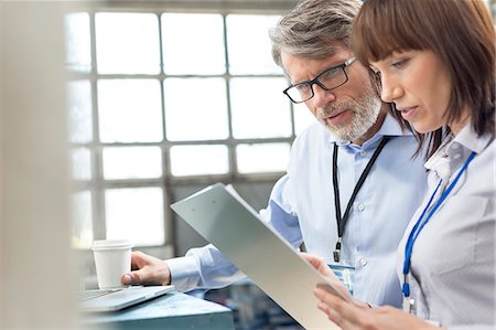 Business people with coffee reviewing clipboard in factory Stock Photo - Premium Royalty-Free, Code: 6113-08393865