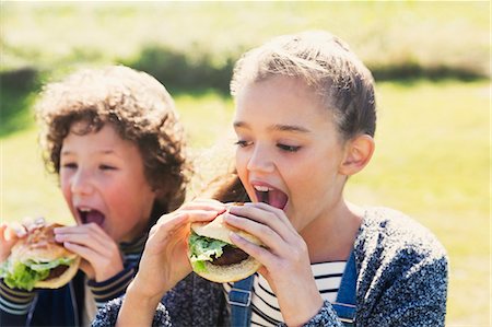 Brother and sister eating hamburgers outside Stock Photo - Premium Royalty-Free, Code: 6113-08393806