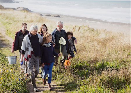 Multi-generation family walking with nets and bucket on sunny grass beach path Photographie de stock - Premium Libres de Droits, Code: 6113-08393810