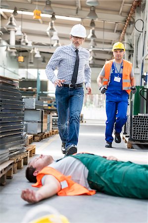Workers running toward fallen coworker unconscious on factory floor Stock Photo - Premium Royalty-Free, Code: 6113-08393836