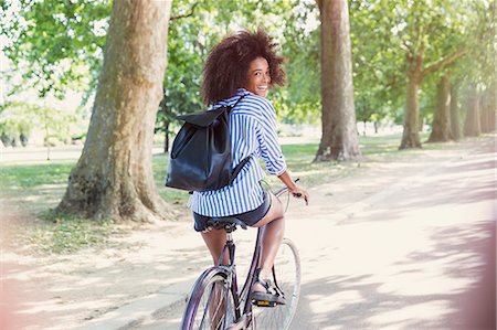 simsearch:6113-08321107,k - Portrait smiling woman with afro riding bicycle in park Photographie de stock - Premium Libres de Droits, Code: 6113-08321095