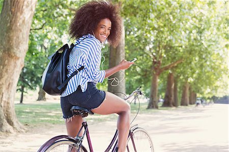 simsearch:6113-08321107,k - Portrait smiling woman riding bicycle with mp3 player and headphones in park Photographie de stock - Premium Libres de Droits, Code: 6113-08321110