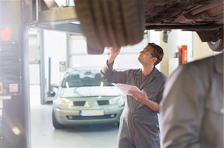 Mechanic with clipboard under car in auto repair shop Stock Photo - Premium Royalty-Free, Code: 6113-08321481