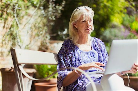 Senior woman using laptop on sunny garden bench Stock Photo - Premium Royalty-Free, Code: 6113-08321563