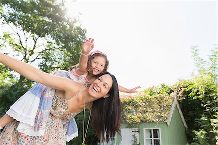 Carefree mother piggybacking daughter with arms outstretched in backyard Photographie de stock - Premium Libres de Droits, Code: 6113-08321590