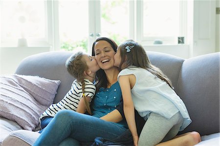 simsearch:6108-06906087,k - Daughters kissing mother's cheeks on living room sofa Stock Photo - Premium Royalty-Free, Code: 6113-08321641