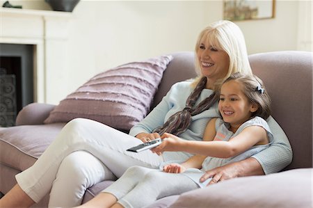 Grandmother and granddaughter watching TV on living room sofa Photographie de stock - Premium Libres de Droits, Code: 6113-08321609