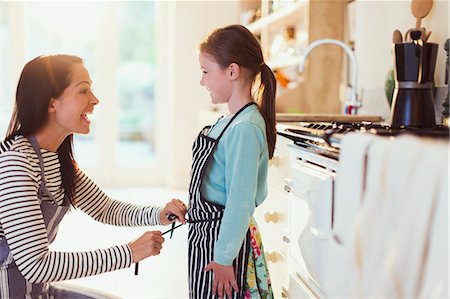 simsearch:6113-08171491,k - Mother tying apron on daughter in kitchen Stock Photo - Premium Royalty-Free, Code: 6113-08321611