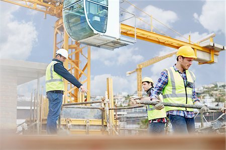 Foreman guiding construction workers below crane at construction site Fotografie stock - Premium Royalty-Free, Codice: 6113-08321777