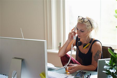 simsearch:6113-08321795,k - Young woman with headphones and tattoo drinking tea and talking on telephone in home office Stock Photo - Premium Royalty-Free, Code: 6113-08321800