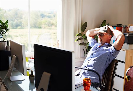 Man leaning back working at computer in sunny home office Foto de stock - Sin royalties Premium, Código: 6113-08321807