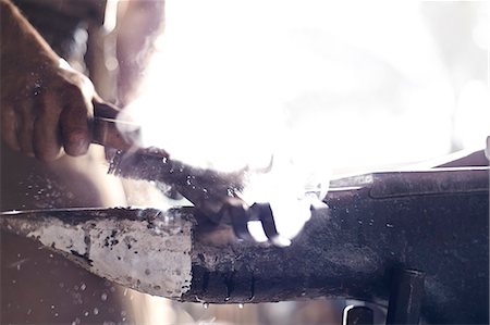 Close up of blacksmith brushing iron tool over anvil in forge Photographie de stock - Premium Libres de Droits, Code: 6113-08424291