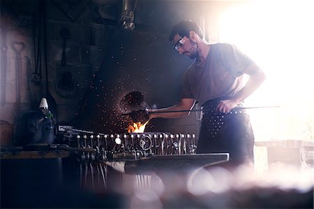 Blacksmith working at fire in forge Foto de stock - Sin royalties Premium, Código: 6113-08424303