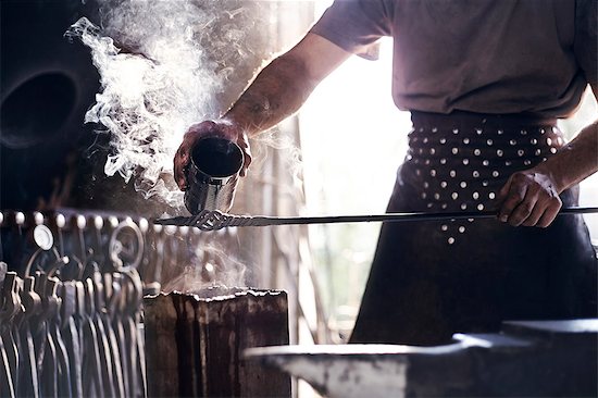 Blacksmith pouring hot liquid over wrought iron in forge Stock Photo - Premium Royalty-Free, Image code: 6113-08424300