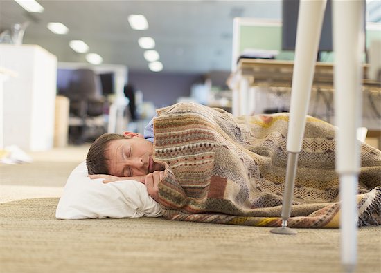 Businessman with pillow and blanket sleeping on office floor Stock Photo - Premium Royalty-Free, Image code: 6113-08549942