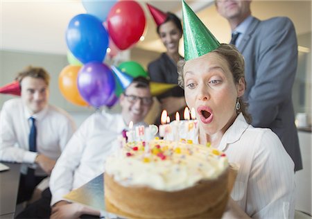 Colleagues watching businesswoman blowing out birthday cake candles Photographie de stock - Premium Libres de Droits, Code: 6113-08549933