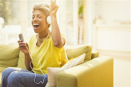 Playful mature woman listening to headphones with MP3 player in living room Photographie de stock - Premium Libres de Droits, Code: 6113-08550046