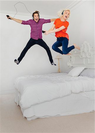 simsearch:632-08698603,k - Portrait playful couple jumping on bed and listening to music with mp3 player and headphones Foto de stock - Sin royalties Premium, Código: 6113-08550057