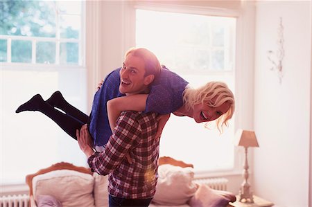 simsearch:6124-08743370,k - Portrait playful husband carrying wife over shoulder in living room Stock Photo - Premium Royalty-Free, Code: 6113-08550059