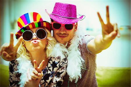 Portrait playful couple in costume sunglasses and hats gesturing peace sign Stock Photo - Premium Royalty-Free, Code: 6113-08550068