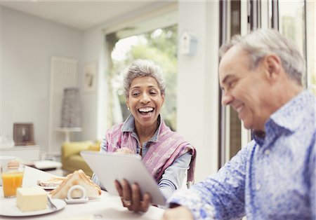 Mature couple laughing and using digital tablet at breakfast table Stock Photo - Premium Royalty-Free, Code: 6113-08550071