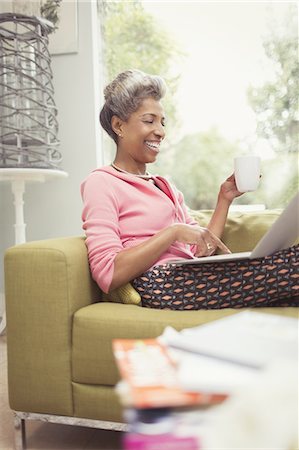 simsearch:695-05771215,k - Smiling mature woman using laptop and drinking coffee on sofa Stock Photo - Premium Royalty-Free, Code: 6113-08550077