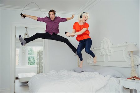 Playful couple jumping on bed and listening to music with mp3 player and headphones Photographie de stock - Premium Libres de Droits, Code: 6113-08550084