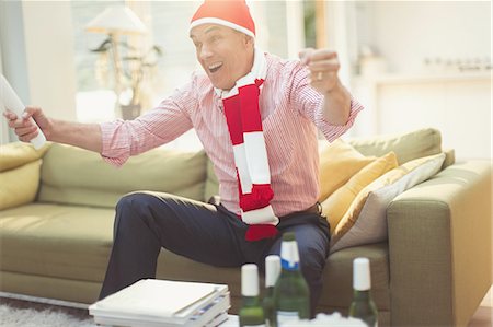 simsearch:614-07146239,k - Enthusiastic mature man in hat and scarf watching TV sports event on living room sofa Stock Photo - Premium Royalty-Free, Code: 6113-08550110