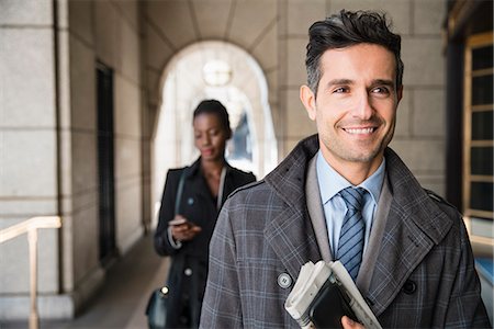 simsearch:693-06435813,k - Smiling corporate businessman carrying newspaper and cell phone in cloister Foto de stock - Sin royalties Premium, Código: 6113-08568675