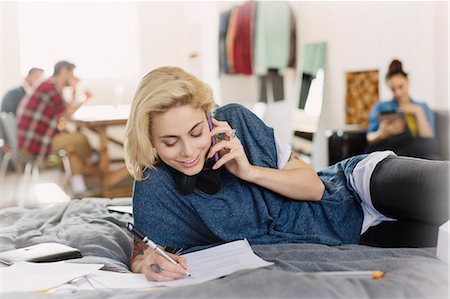 Female college student studying and talking on cell phone on bed Stock Photo - Premium Royalty-Free, Code: 6113-08568613