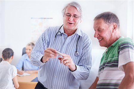 Doctor showing senior man digital thermometer at checkup Foto de stock - Royalty Free Premium, Número: 6113-08568740