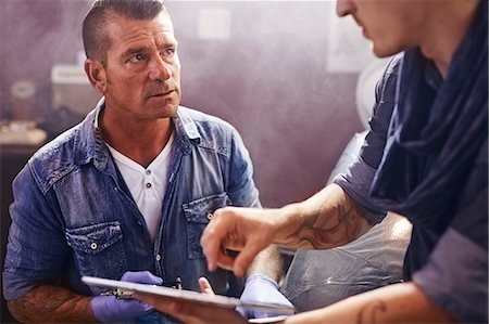 Man with digital tablet talking to tattoo artist Stock Photo - Premium Royalty-Free, Code: 6113-08521278