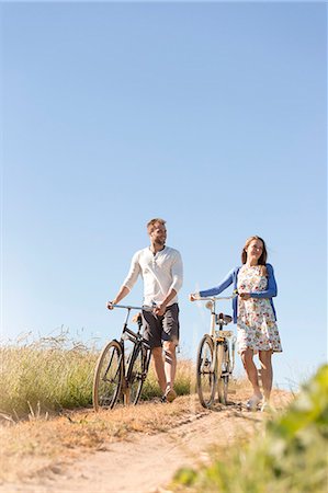 Young couple walking bicycles on dirt road below sunny blue sky Stock Photo - Premium Royalty-Free, Code: 6113-08521532