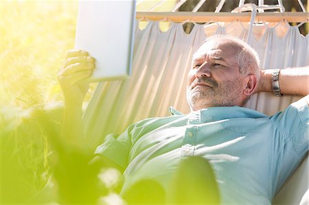 senior man digital tablet - Senior man using digital tablet and relaxing in summer hammock Foto de stock - Sin royalties Premium, Código: 6113-08521534