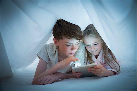 reading to kids - Brother and sister sharing digital tablet under sheet Stock Photo - Premium Royalty-Free, Code: 6113-08655375