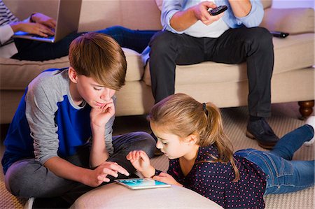 family playing games indoors - Brother and sister sharing digital tablet in living room Stock Photo - Premium Royalty-Free, Code: 6113-08655383