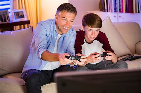 Father and son playing video game in living room Stock Photo - Premium Royalty-Free, Code: 6113-08655389