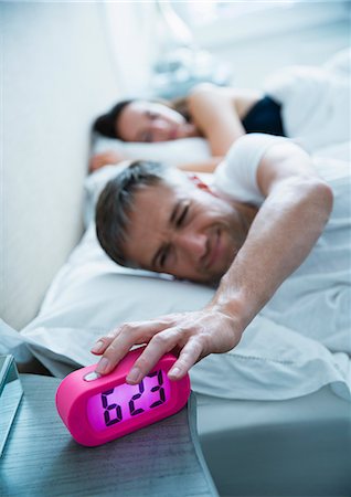 simsearch:6113-08655424,k - Man in bed turning off morning alarm clock Foto de stock - Sin royalties Premium, Código: 6113-08655440