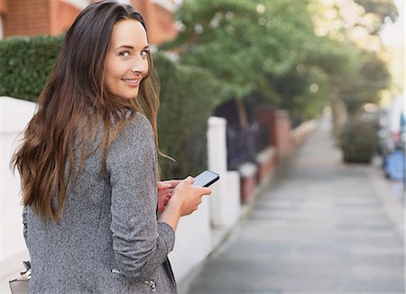 rear view of woman texting cellphone - Portrait smiling businesswoman with cell phone looking back on sidewalk Stock Photo - Premium Royalty-Free, Code: 6113-08655451