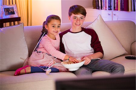 Brother and sister eating popcorn and watching TV in living room Stock Photo - Premium Royalty-Free, Code: 6113-08655416