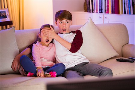 family watching tv surprised - Brother covering surprised sister's eyes watching TV in living room Stock Photo - Premium Royalty-Free, Code: 6113-08655438