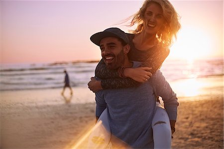 Playful couple piggybacking on sunset beach Foto de stock - Sin royalties Premium, Código: 6113-08655554