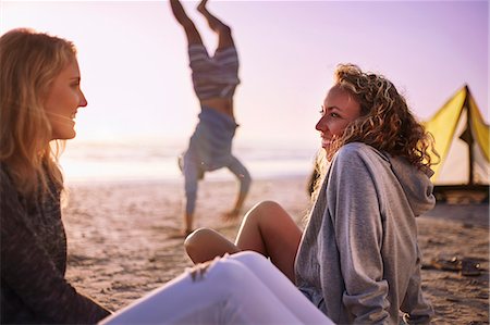 Smiling women talking on beach with man doing handstand in background Stock Photo - Premium Royalty-Free, Code: 6113-08655527