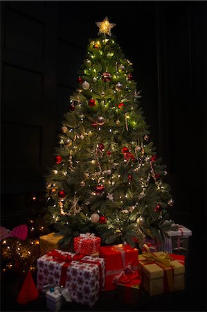 Illuminated Christmas tree surrounded by gifts in dark room Foto de stock - Sin royalties Premium, Código: 6113-08659593